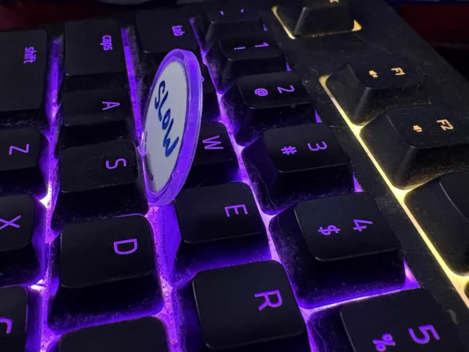 A photo of a keyboard with an InfiniTokens dry erase counter wedged in front of the 'W' key to hold it down.  