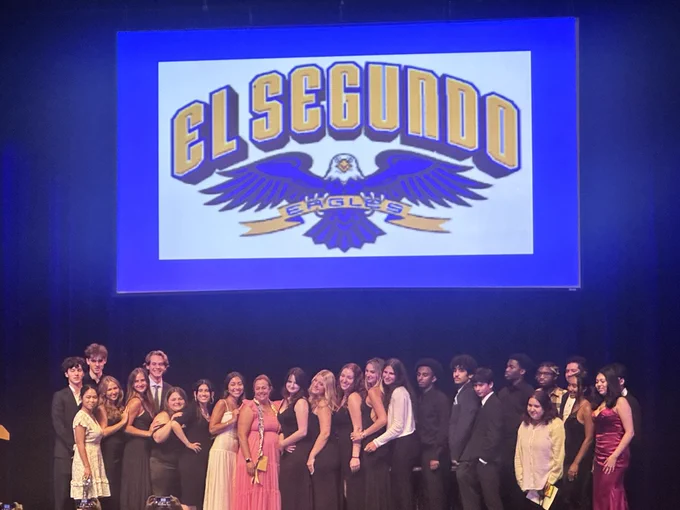 Group of young adults dressed formally posing on stage under a large El Segundo Eagles logo projection.