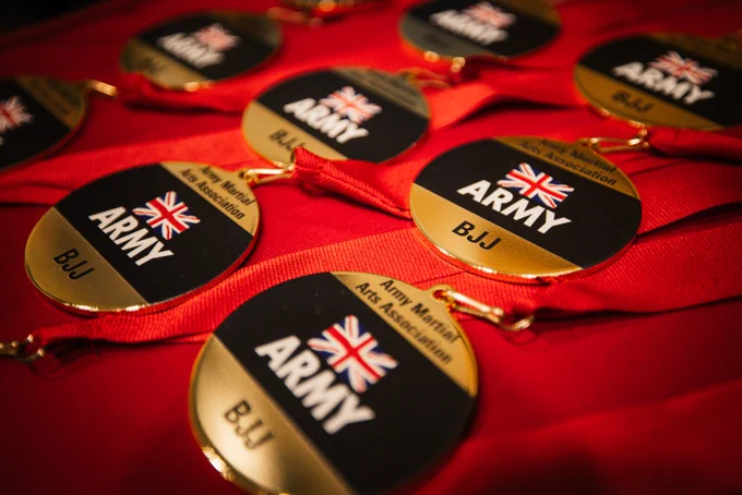 Gold medals with "Army" and "BJJ" text, featuring a Union Jack flag, are displayed on a red surface.