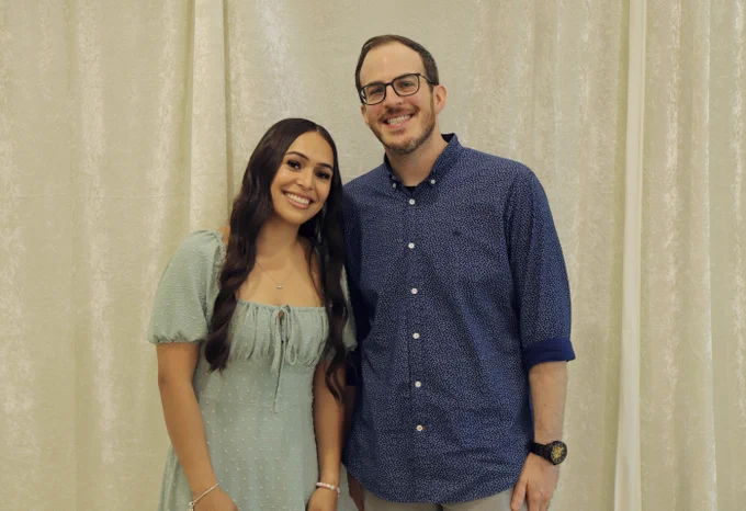 A man and a woman stand smiling at the camera. 