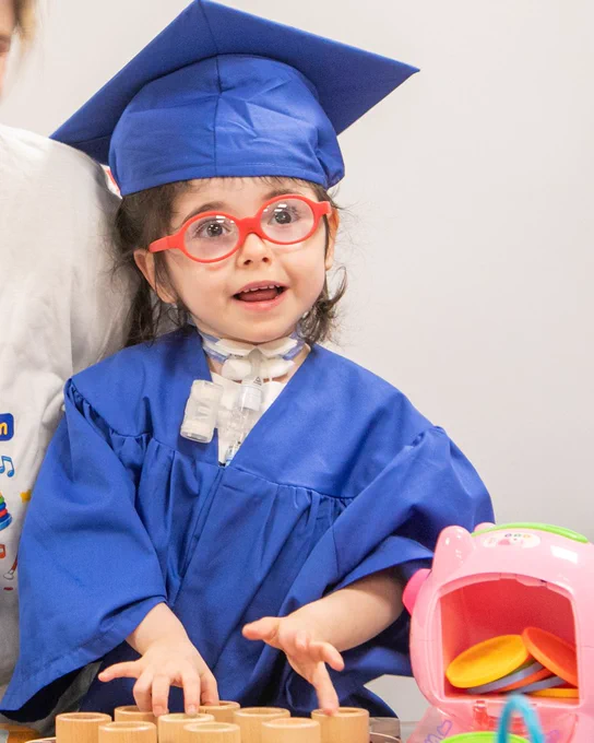 Isabella wearing a blue cap and gown, and bright red glasses, smiling at the camera
