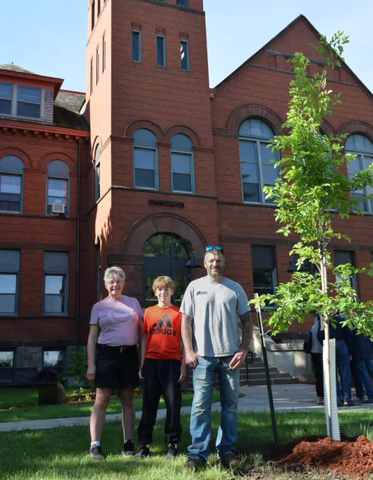 Larry's wife, grandson and son standing by the newly planted tree in front of McFarland Hall