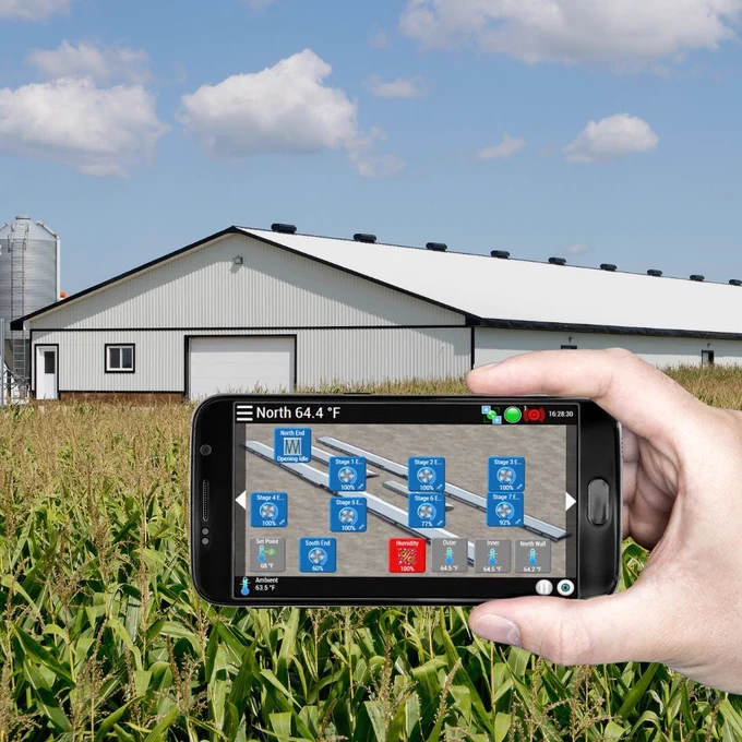 Hand holding a smartphone displaying AutoFlex Connect barn monitoring controls in front of a livestock barn and corn field showing remote ventilation and environmental management features.
