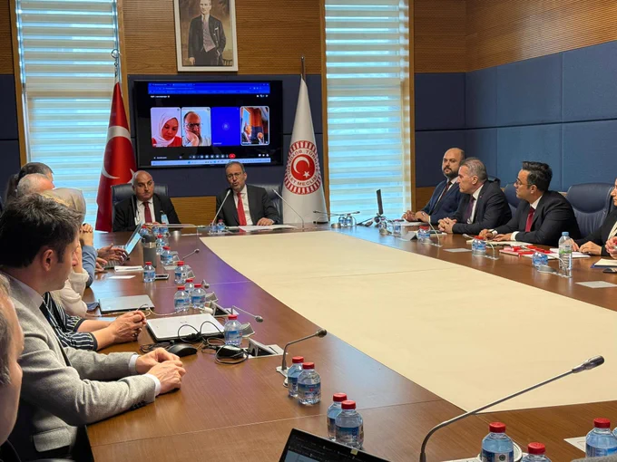 TBMM’de gerçekleştirilen toplantıda Komisyon Başkanı Mehmet Muharrem Kasapoğlu başkanlığında uzmanlar, akademisyenler ve davetlilerin katılımıyla komisyon raporunun yazım süreci değerlendiriliyor. Uzun toplantı masasının etrafında bir araya gelen katılımcılar istişareleri takip ederken, arka plandaki ekranda çevrim içi bağlantıyla toplantıya katılan uzmanlar görülüyor.