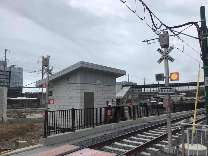 Railroad crossing with warning lights and a small building beside the tracks under a cloudy sky.