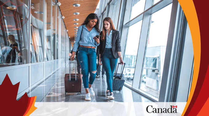 Deux femmes traversent un terminal d'aéroport en tirant des valises à roulettes et en regardant ensemble un smartphone.
