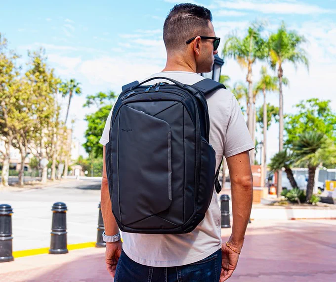 Casual dressed individual seen from behind, sporting a modern black Targus Pro-Tek Tech Backpack in a bright urban setting.