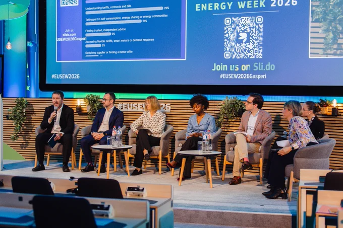 A panel discussion at the European Sustainable Energy Week 2026, featuring multiple speakers sitting on a stage with a screen in the background displaying information related to the event