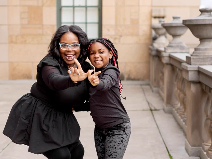 A returning adult student and her daughter pose holding their fingers up in the shape of a W, each making one half of the W.