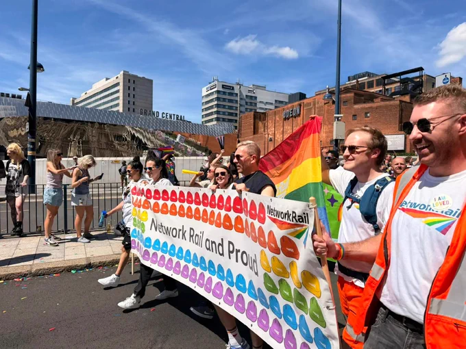 A group of people marching in a pride parade, holding a banner that reads "Network Rail and Proud" with colorful heart designs. 
