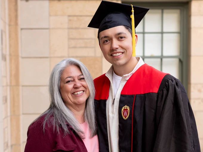 A returning adult student wearing a graduation cap and gown poses for a picture with his mother.