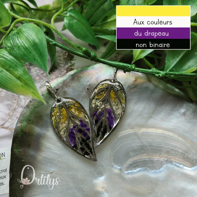 Boucles d'oreilles argentées en forme de feuilles, entre les ramures des pétales de fleurs jaunes, blanches, violettes et noires,  rappelant les couleurs du drapeau non binaire