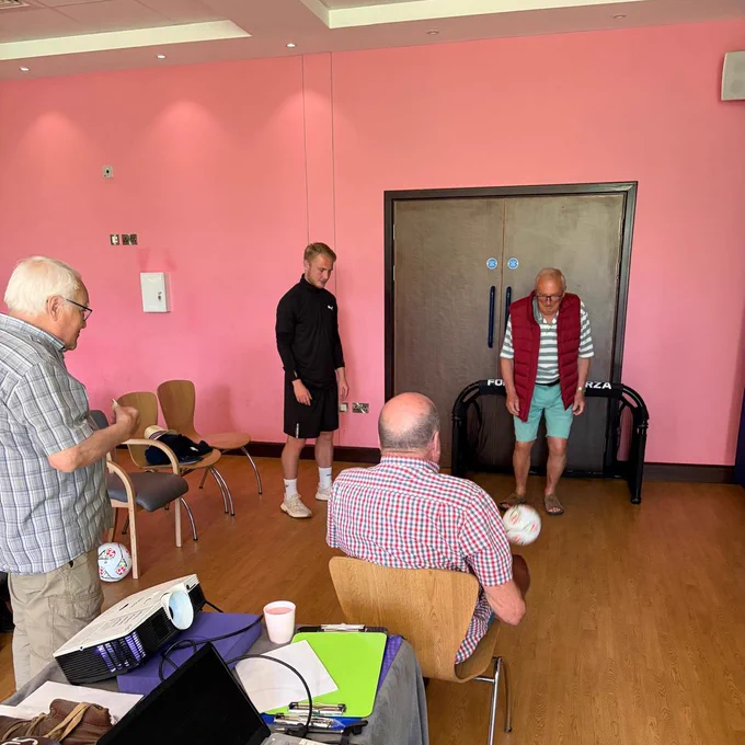 Liam Bennett supporting two Sporting Memroies members pass a football between each other.