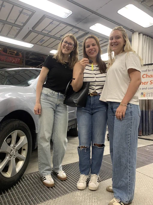 Three ladies with one of them holding a car key happy about the new look of their car. 