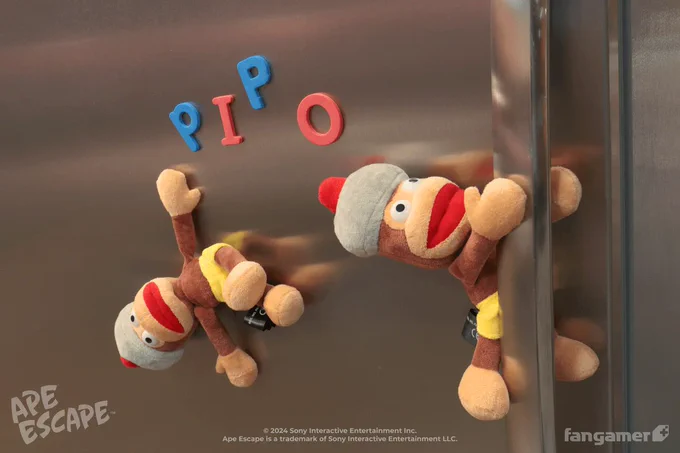 A photo of two Pipo Monkey plushes from our Ape Escape collection hanging on the Fangamer freezer using their magnetic hands and feet. P I P O is spelled out with refrigerator magnets. 