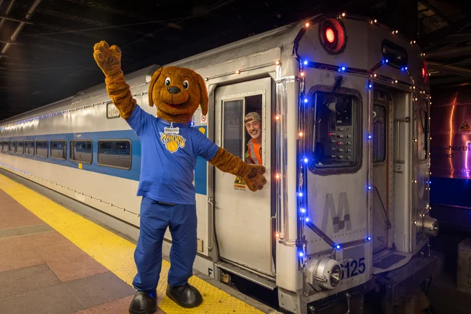Tracks the Dog waving next to the orange and blue lights train. 