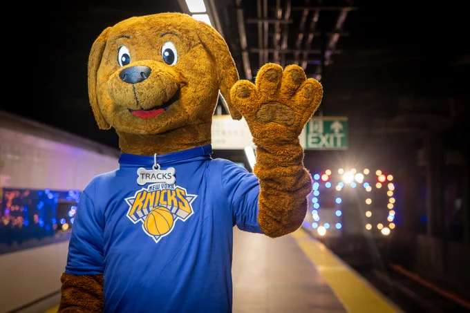 Tracks the Dog in a Knicks shirt with an orange and blue lights train in the background.