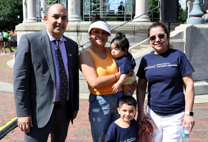 A group of adults with two small children smiles for a photo in front of a large statue in a park setting.