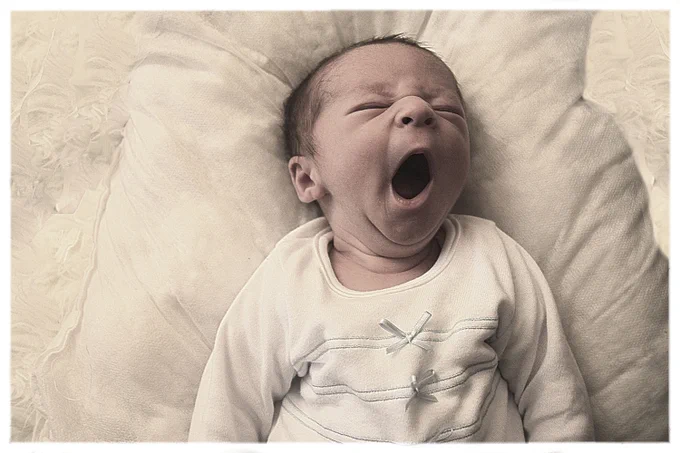 Newborn baby wearing a white outfit yawns.