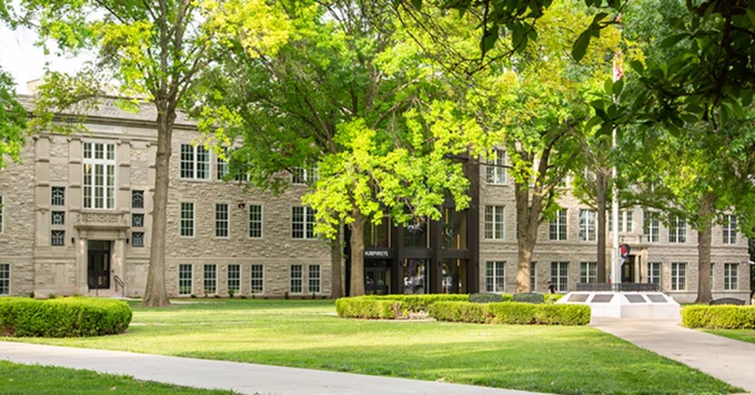 A wide view of a Humphreys building framed by lush green trees, manicured hedges, and a grassy lawn with walkways.