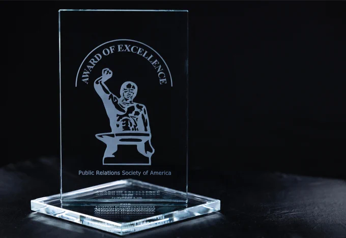 Rectangular, flat crystal award with engraved "Anvil Award of Excellence", an image of blacksmith with raised hammer over an anvil and "Public Relations Society of America"