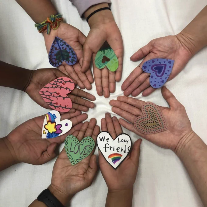 Multiple hands holding colorful heart-shaped crafts in a circle.