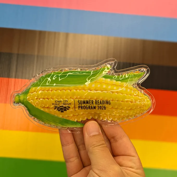 A hot and cold pack shaped like a corn with text that reads "Iowa City Public Library Summer Reading Program 2026"