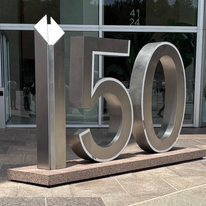 a steel sculpture that says “150” in which the 1 is a model of the rectangular building with a diagonal roof it’s in front of