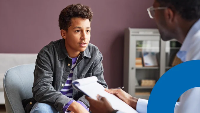 A young person speaks with a healthcare professional during a supportive conversation in a clinical setting.