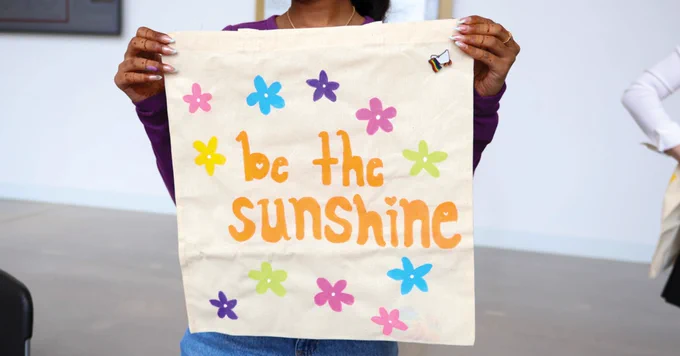 A person holding a canvas bag with colorful flowers surrounding the phrase "be the sunshine.