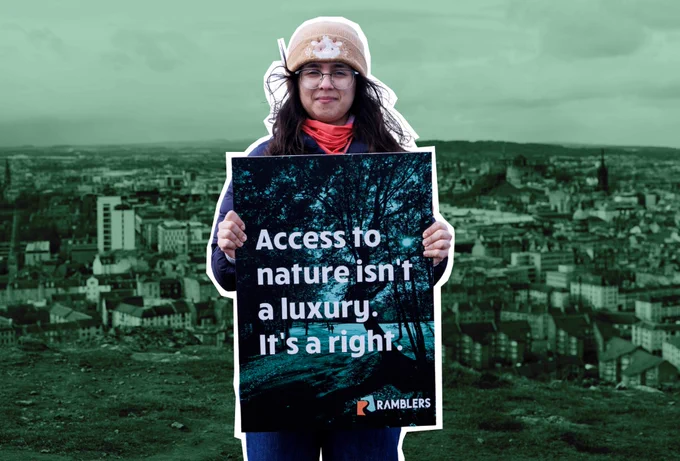 A person outdoors holds a sign reading, "Access to nature isn't a luxury. It's a right." The background shows an urban landscape. The logo of "Ramblers" is visible on the sign.