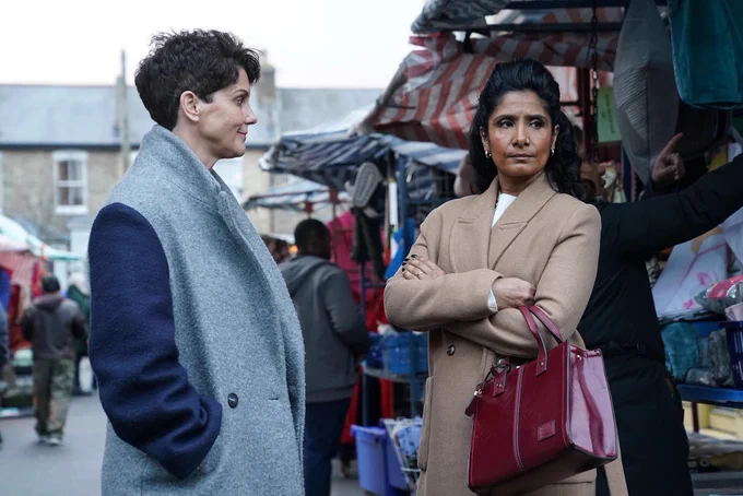 Suki and Eve Panesar-Unwin stood in the market in EastEnders, with Suki having arms crossed and looking concerned.