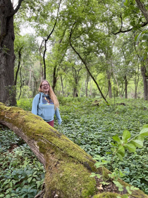 Alex Rinehart smiles in a wooded area next to a fallen tree.