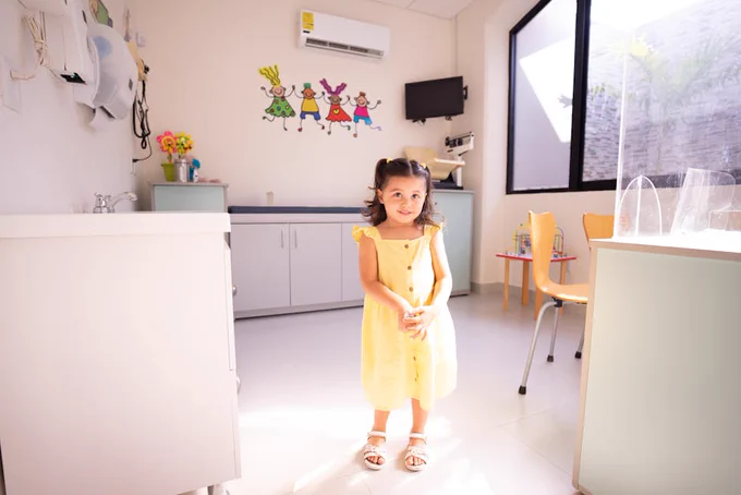 Adorable child smiling in a bright medical clinic, wearing a yellow dress and enjoying a sunny day.