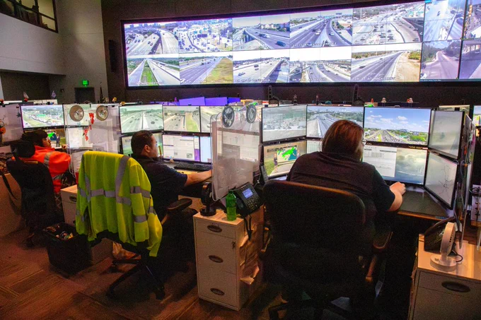 Traffic control center operators monitor multiple screens showing live highway footage to manage road conditions and incidents.