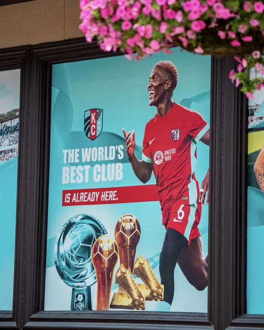 Window of the Current Shop with signage that reads "the world's best club is already here" with a photo of Temwa and the Shield along with her two MVPs & two Golden Boot trophies 