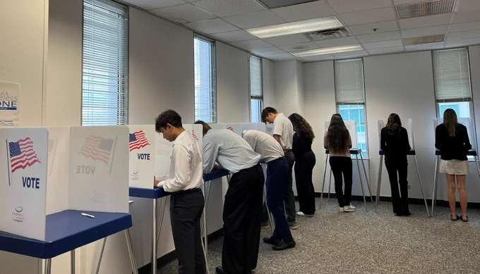 A group of people standing at voting booths in a well-lit room casting their ballots during an election.