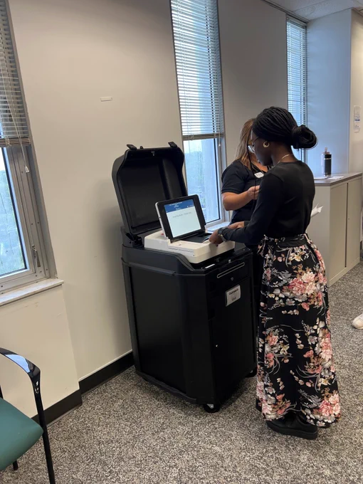 Woman in floral skirt casting her ballot in a tabulator after voting.