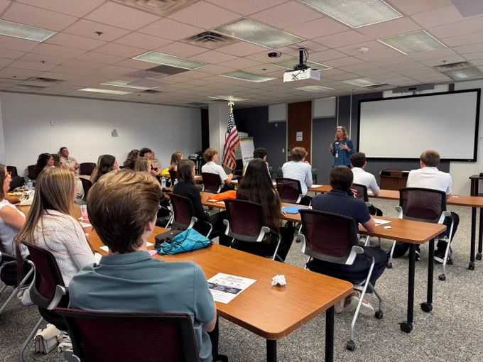 Supervisor of Elections, Melissa Blazier, giving a presentation to a diverse group of attentive adults seated in a classroom.