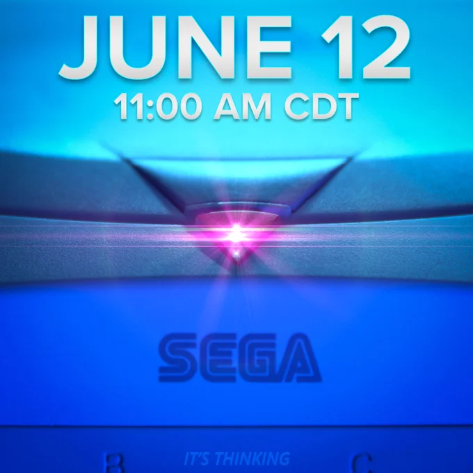 A close-up shot of the red, triangular Sega Dreamcast power light. The Dreamcast is lit in dark blue lighting with the Sega logo visible near the bottom. The red power light is emitting a lens flare. Silver text above says: June 12, 11:00 AM CDT. Small text near the bottom says: It's Thinking.