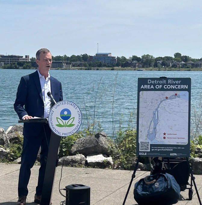 EGLE Director Phil Roos standing next to poster on easel at Detroit River Area of Concern event speaking to audience.