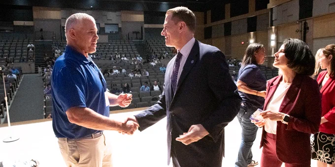 Dr. Taylor shaking hands with retiree on a stage in a large auditorium with scattered audience members in the background.
