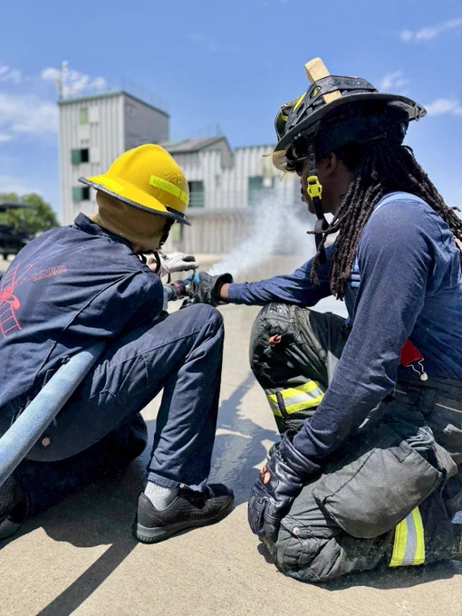 Daytime image of a firefighter showing a teen how to use a fire hose