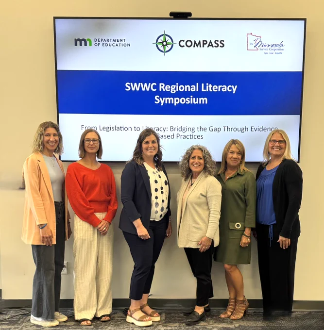 Literacy Director Julie Novak and Literacy
Specialist Jenny Wazlawik stand with Southwest Service Cooperative
Literacy Team members Natalie Delmonico, Shannon Gossen and Ginny Sorenson and
COMPASS Supervisor Allyson Pesek in front of a PowerPoint display that reads SWWC Regional Literacy Symposium. From Legislation to Literacy: Bridging the Gap Through Evidence Based Practices.
