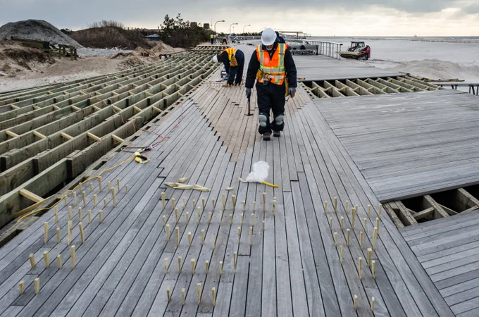 Construction workers in safety gear making repairs to a boardwalk at Jones Beach State Park in Long Island, New York.