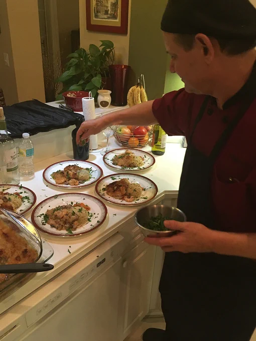 A chef in a red uniform garnishes plates with herbs in a cozy kitchen. The setting conveys a warm and inviting atmosphere.