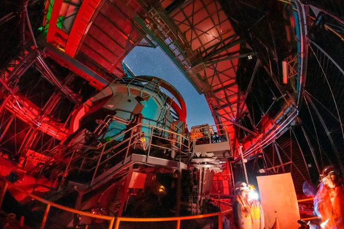 The view from inside NSF–DOE Vera C. Rubin Observatory. The Simonyi Survey Telescope points upwards towards the opening in the observatory's dome through which the night sky is visible.