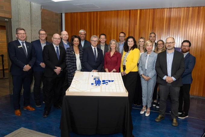 PCL Construction team and project partners standing behind a table with a site model at NAIT Advanced Skills Centre announcement in Edmonton, Alberta.