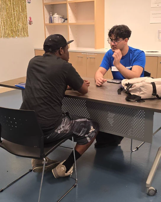 A volunteer and client are sitting across a table. The volunteer is listening intently to the client speak. 