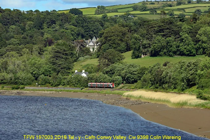Transport for Wales, TFW, train no 197003 travels alongside the River Conway valley towards Tal -y - Cafn Station in in North Wales. 
The service it is working is the 16.10 hrs train from Llandudno to Blaenau Ffestiniog.
The road that crosses the railway here on a level crossing is the B5279 and just beyond this level crossing is the Tal -y – Cafn bridge, the first crossing point of the River Conwy outside of the town of Conwy itself. 
The river Conwy is 34 miles long, discharging into the Irish sea. It is tidal past Tal - y - Cafn up to Llanrwst. 
This railway line runs up the east side of the Conwy valley from Llandudno junction and the North Wales main line to Blaenau Ffestiniog. It is mainly a single-track rural branch line. 
Tal -y - Cafn station is a request stop, meaning passengers need to tell the guard if they want to get off, or signal the driver to stop if they want to board the train. 
This a Wednesday service on the 10th June 2026.
 mage Cw 9398 Copyright Colin Wareing